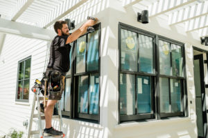 A technician installs Pella replacement windows with black frames on a single-family home.